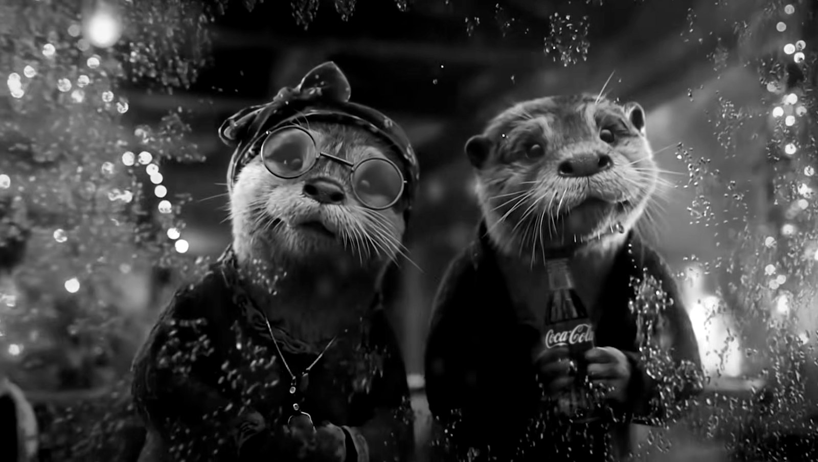Still from Coca-Cola “Holidays Are Coming”: two otters in winter clothes, one holding a Coca-Cola bottle