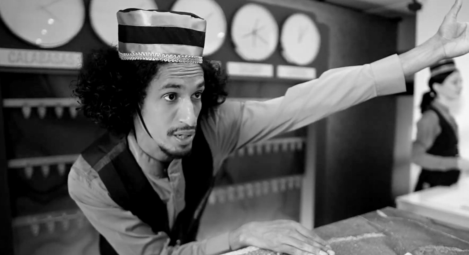 Still from Hulu “Motel”: a costumed desk clerk gesturing across the front desk
